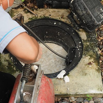 Drain cleaning. Plumber repairing clogged grease trap with auger machine. Maintenance the sewage system and grease trap by professional plumber. Using auger snake to fix and unclog a drain.